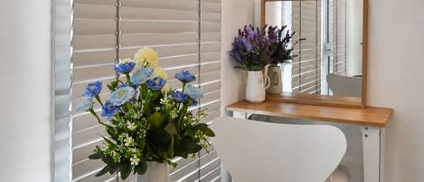 Ett rum med ett runt bord, en vas med blommor, en spegel och en väggmonterad lampa.
