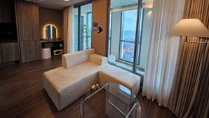 A modern living room with a sofa, a glass coffee table, and a view of the city through large windows. - Haeundae Lamer Stay (Busan)