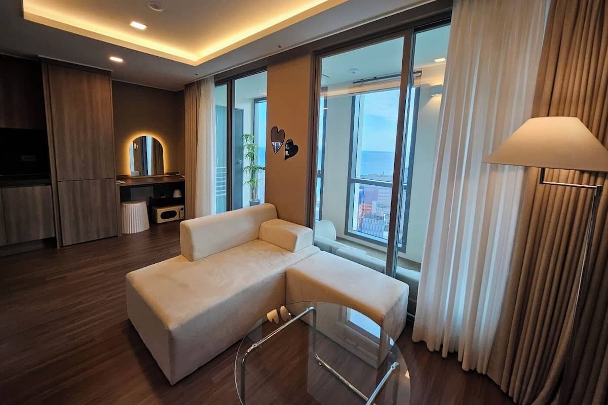 Una sala de estar moderna con un sofá, una mesa de centro de vidrio y vistas de la ciudad a través de amplias ventanas.