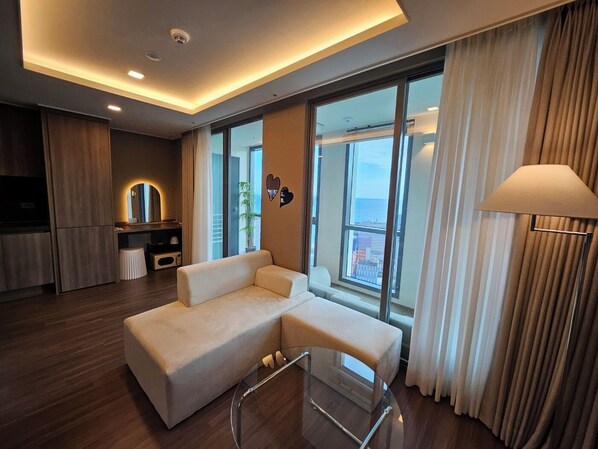 A modern living room with a sofa, a glass coffee table, and a view of the city through large windows.