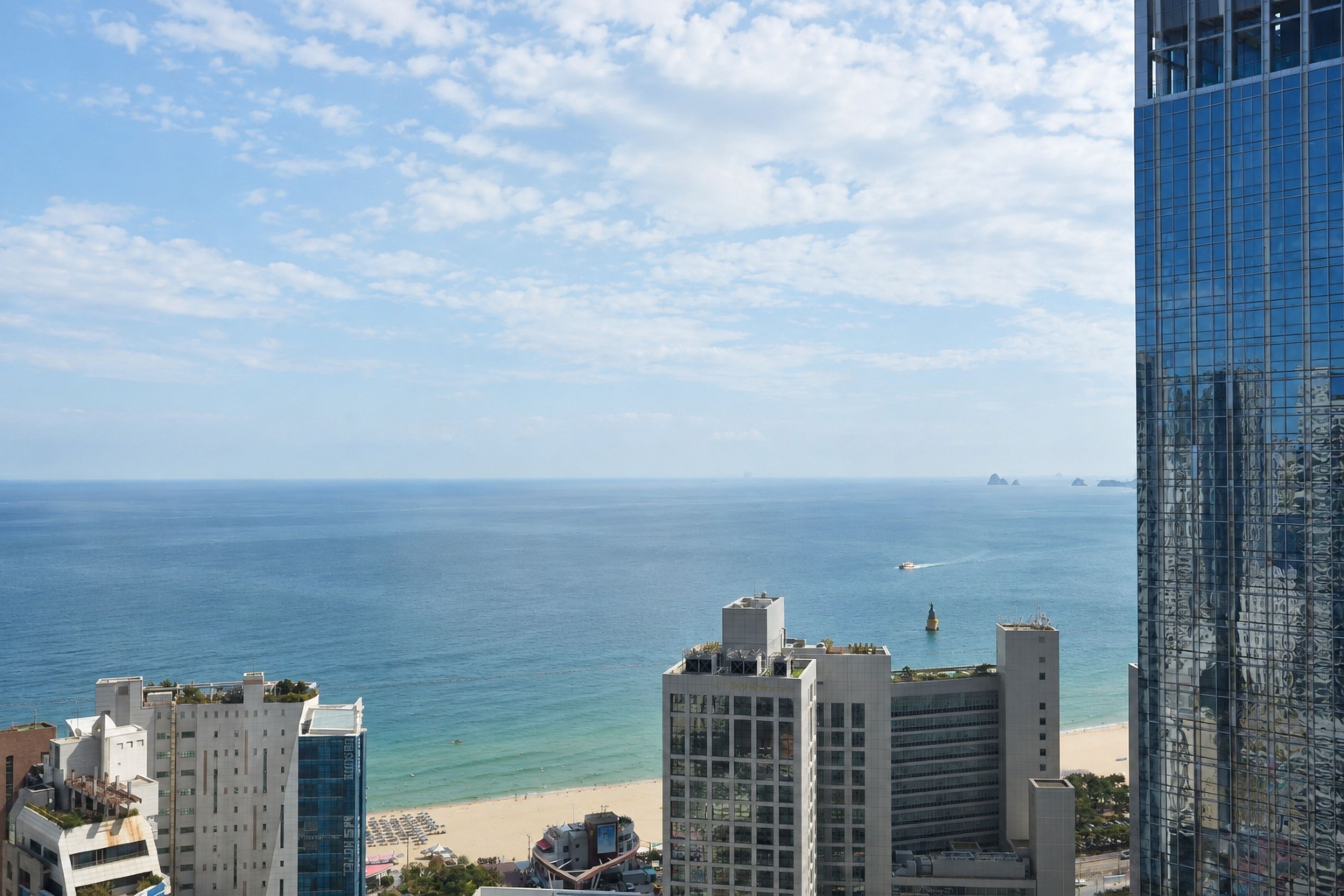 A coastal cityscape with modern buildings, a beach, and a clear sky.