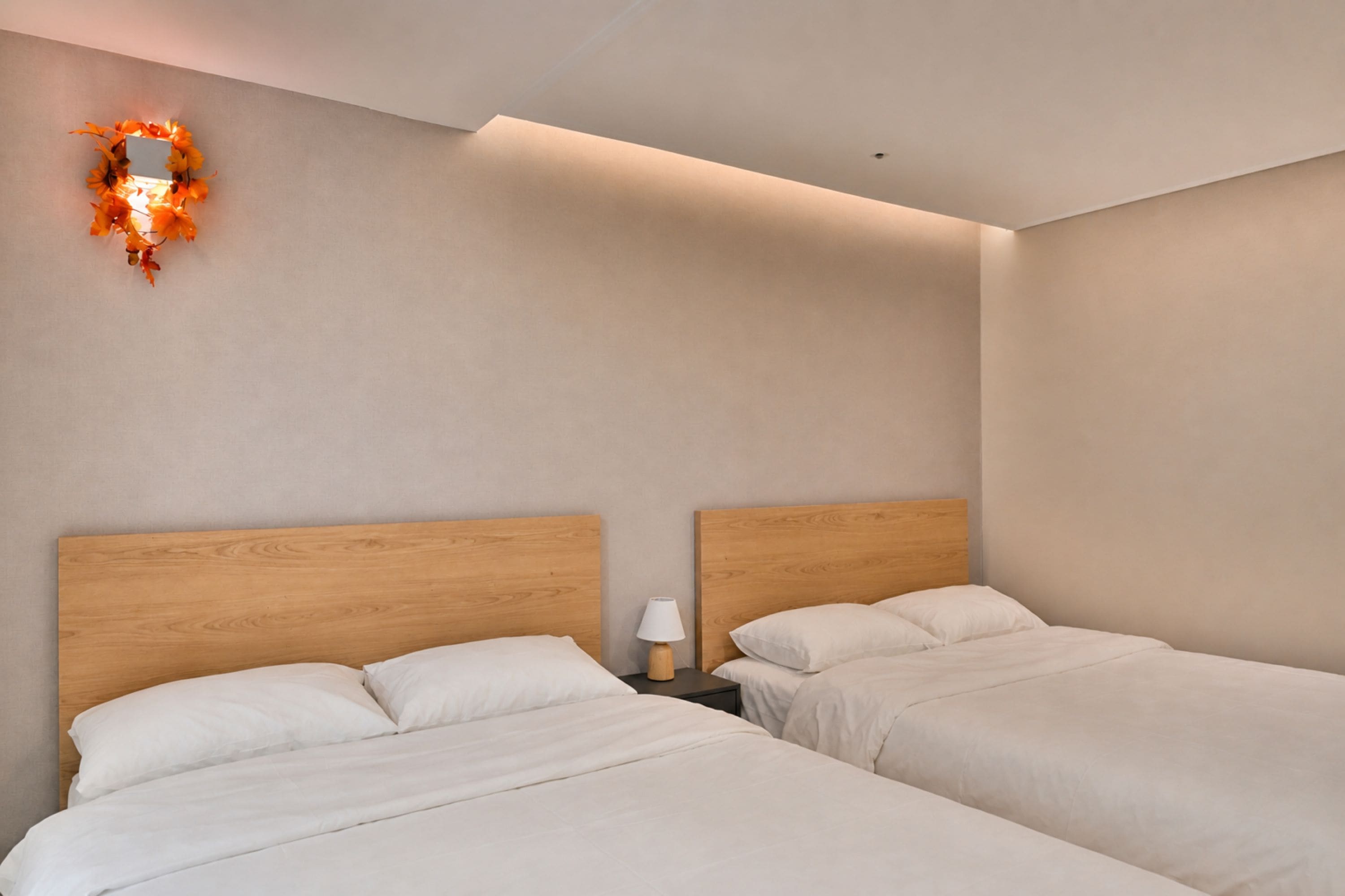 A hotel room with two beds, a nightstand, a wall-mounted light fixture, and a ceiling light.