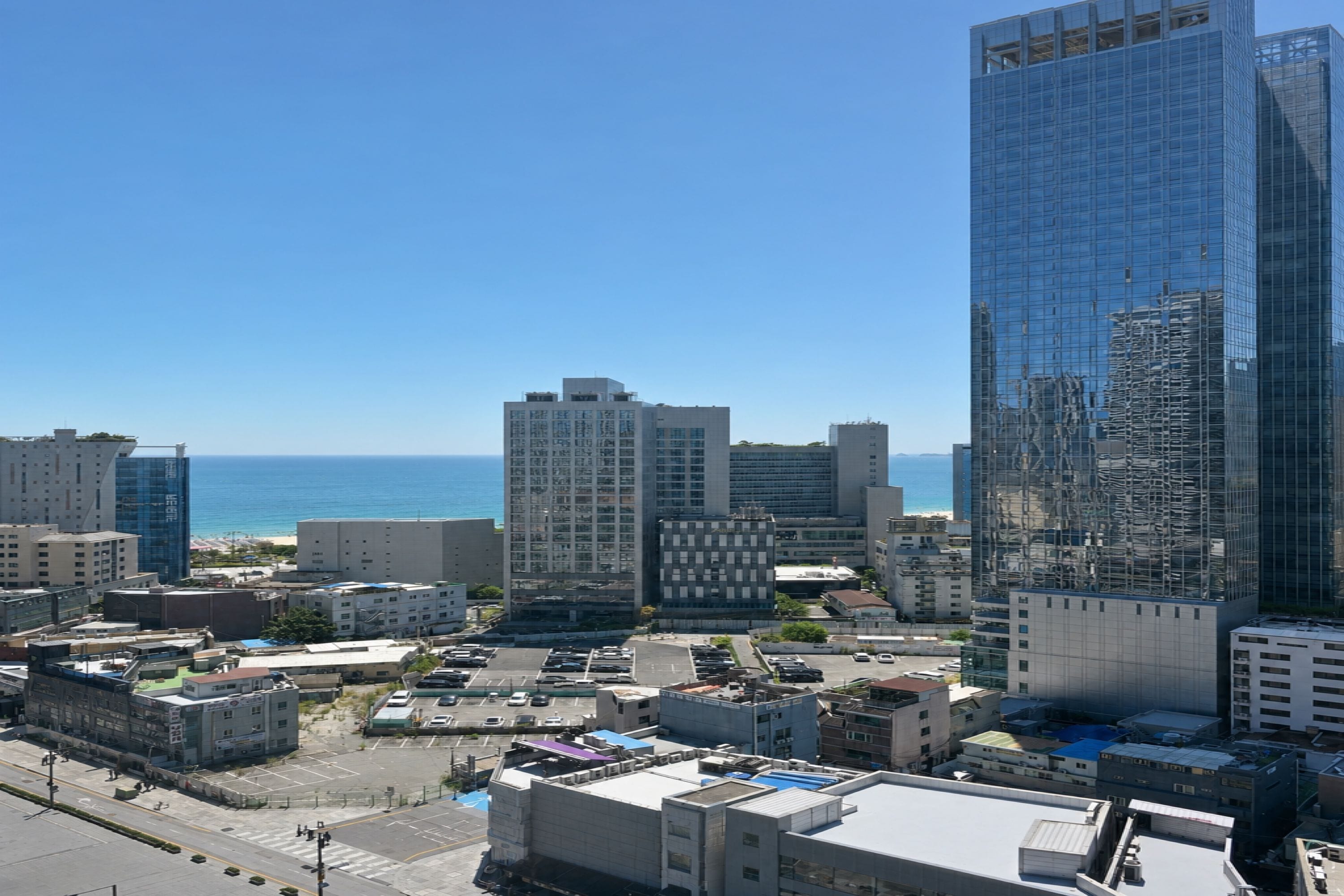 A cityscape with modern buildings, a clear sky, and a view of the ocean.