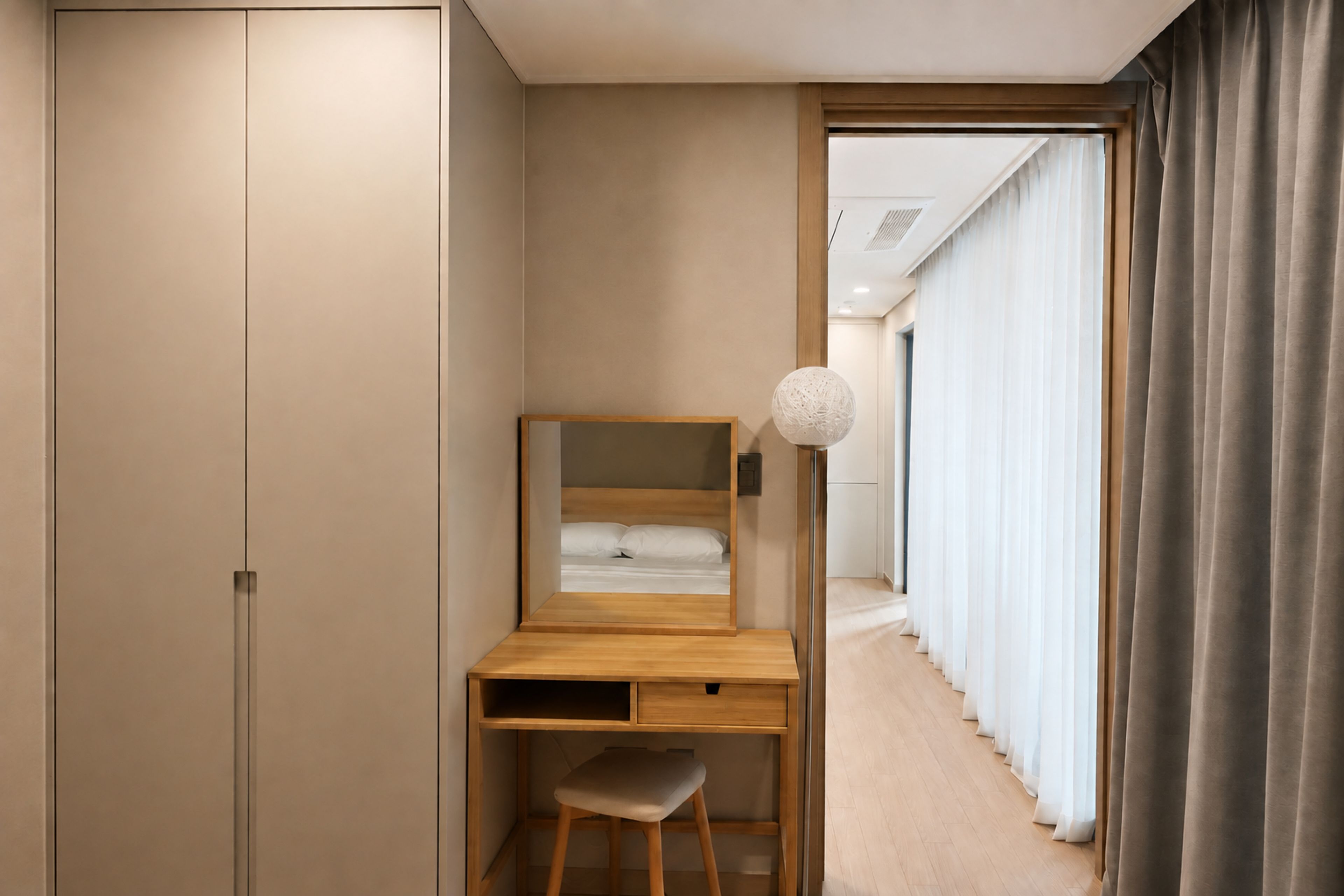 A bedroom with a wooden desk, a chair, a bed, and a large window with curtains.