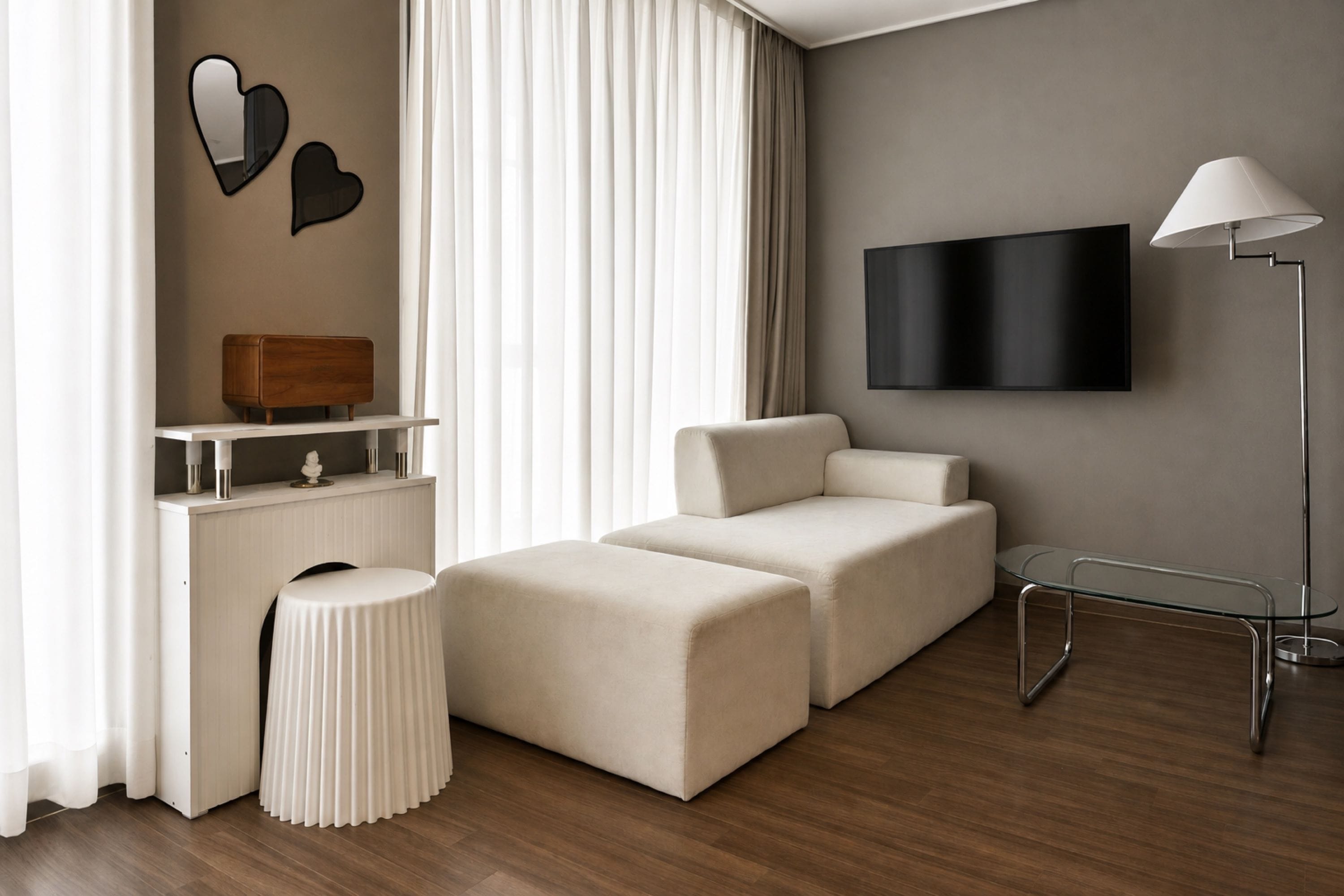 A modern living room with a sofa, ottoman, and a flat-screen TV mounted on the wall.