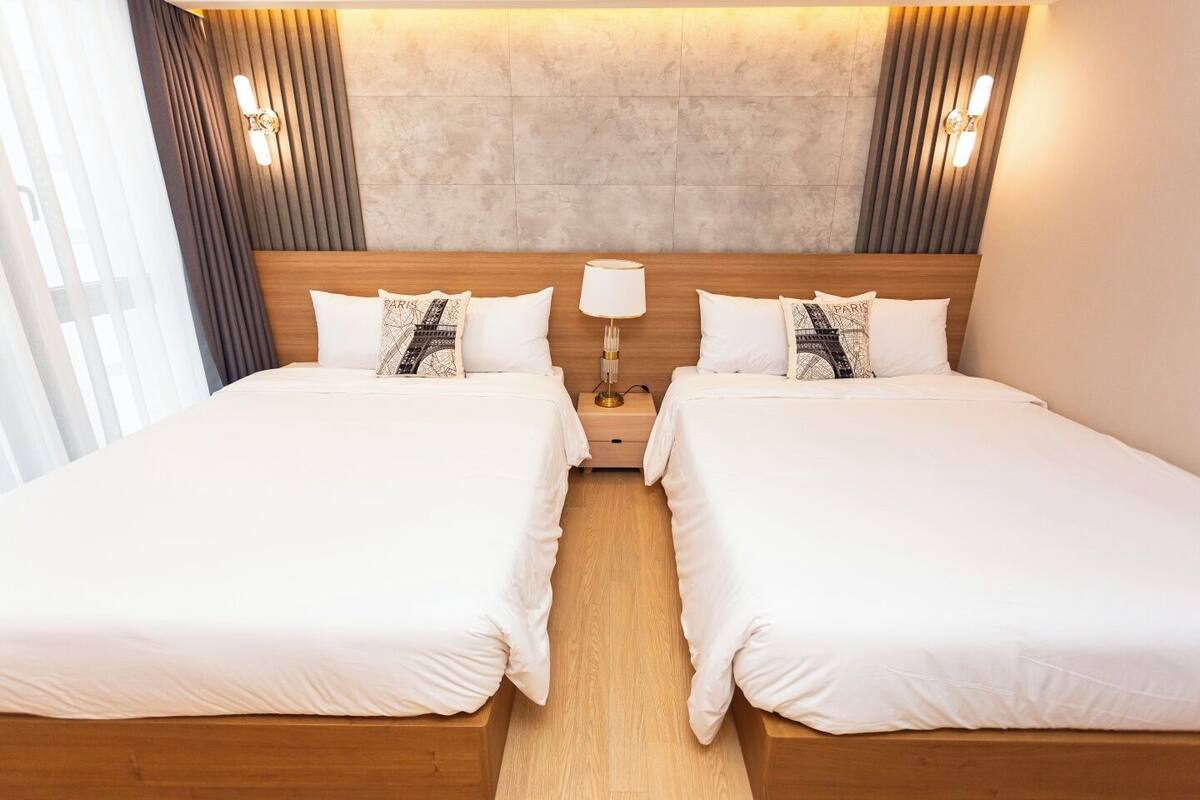 Habitación doble con cama y cabecera de madera, dos mesitas de noche con lámparas y almohadas decoradas con motivos de la Torre Eiffel.