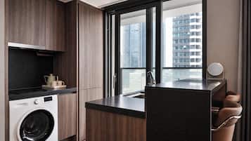 A modern kitchen with a built-in washer, a large window with a city view, and a small seating area with a mirror.