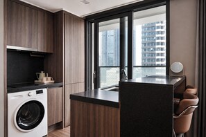 A modern kitchen with a built-in washer, a large window with a city view, and a small seating area with a mirror.