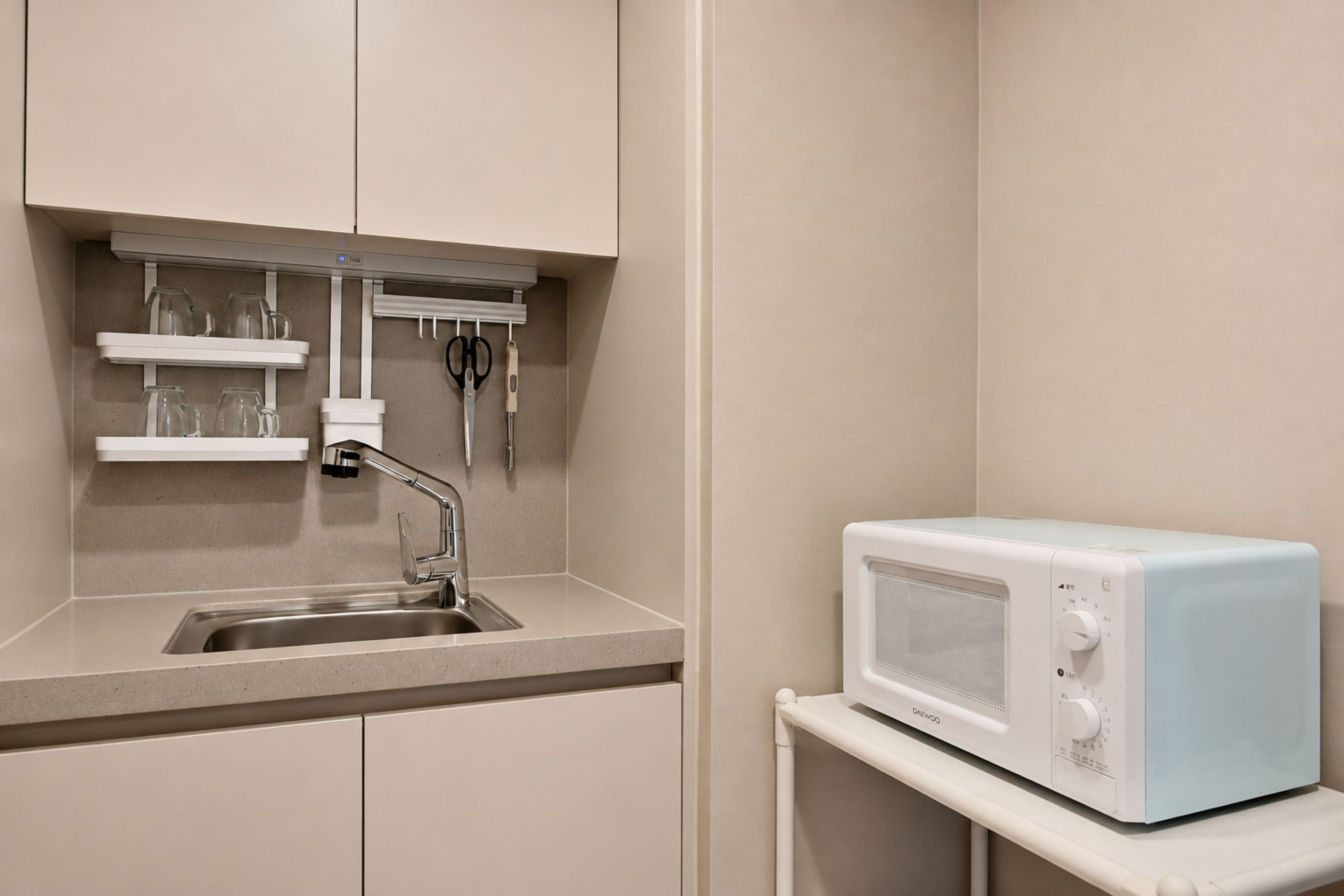 Een kitchenette met een inbouwmagnetron, een spoelbak en een plank met glazen en bestek.