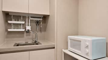 Una kitchenette equipada con microondas, pileta y un estante con cristalería y utensilios.