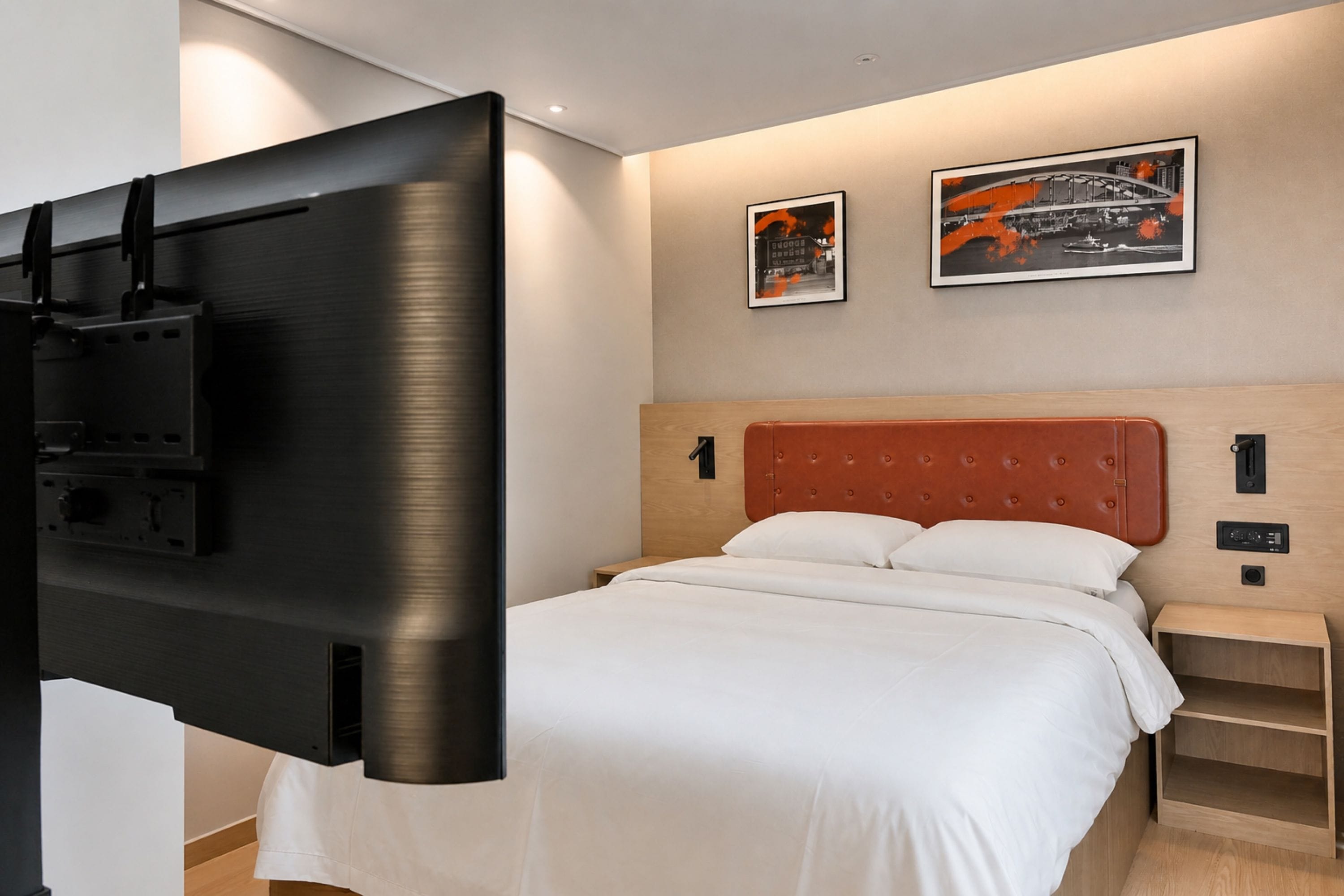 Una habitación de hotel con una cama, un televisor montado en la pared y dos cuadros enmarcados.