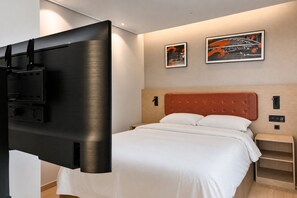 A hotel room with a bed, a TV mounted on the wall, and two framed pictures on the wall.