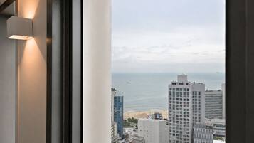 A view of a coastal cityscape through a window, featuring high-rise buildings, a beach, and the ocean.