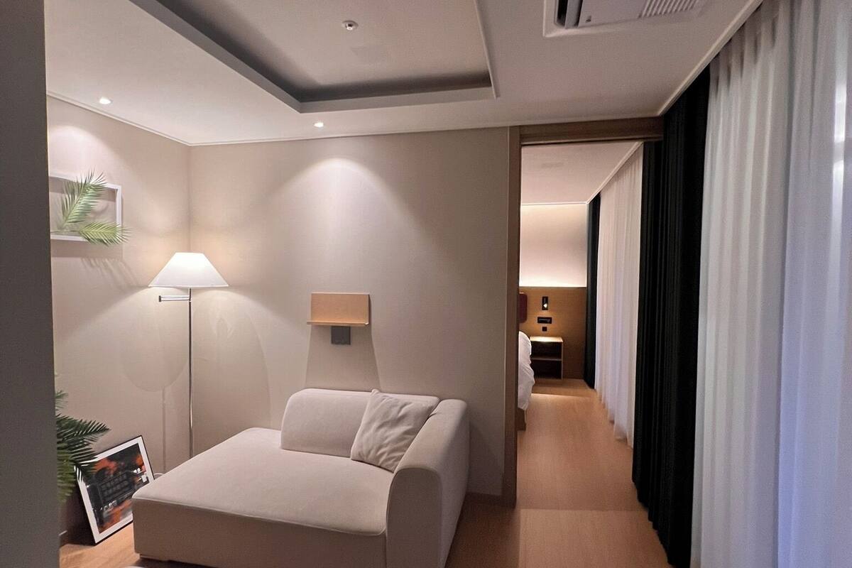 Una habitación de hotel moderna con sofá, una mesita, una lámpara y vista al pasillo.