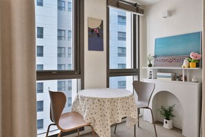 Una camera d'albergo con un tavolo rotondo, due sedie, una grande finestra e un quadro appeso al muro.