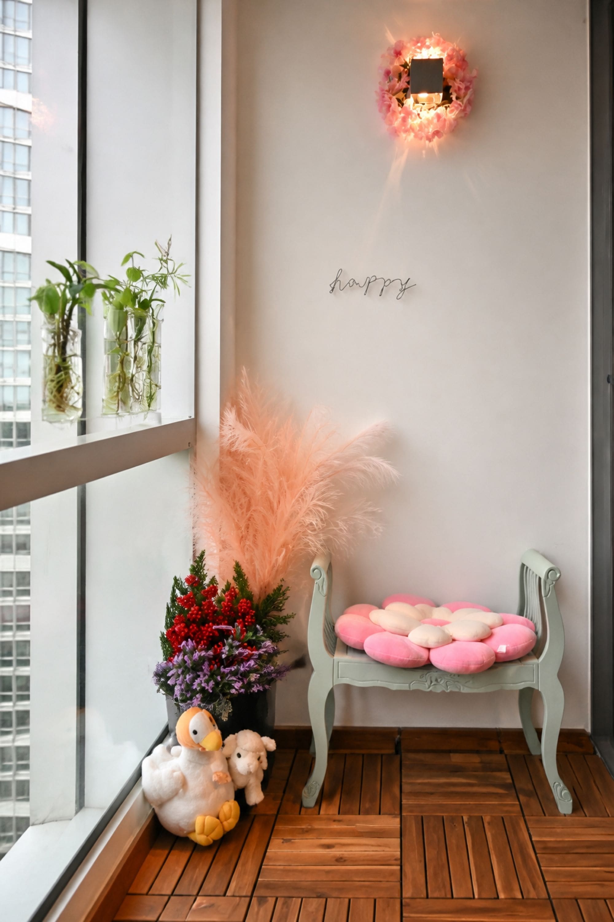 A balcony with a wooden floor, a decorative wall with a light fixture, a bench with cushions, and potted plants.