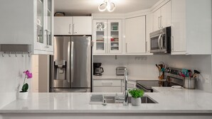 Una cocina moderna con armarios blancos, electrodomésticos de acero inoxidable, cafetera y lavamanos.