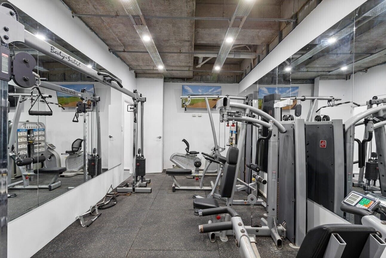 Une salle de sport équipée de divers appareils d’exercice, de miroirs et dotée d’un plafond en béton.