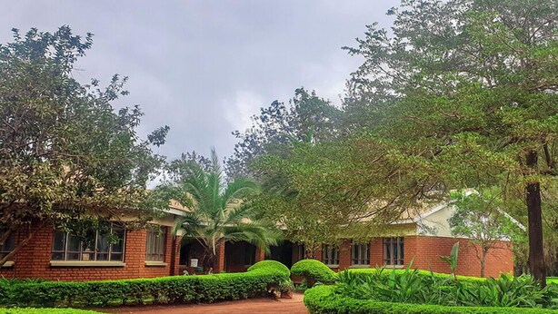 A brick building with a paved pathway, surrounded by well-maintained hedges and trees. - KLH RESORT (Karatu)