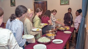 A group of people standing around a table with various dishes, likely at a communal meal. - KLH RESORT (Karatu)