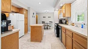 A modern kitchen with wooden cabinets, a central island, and a dining area with chairs and a table.