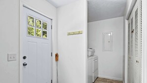 A clean, white-walled hallway with a door, a window, and a laundry area.