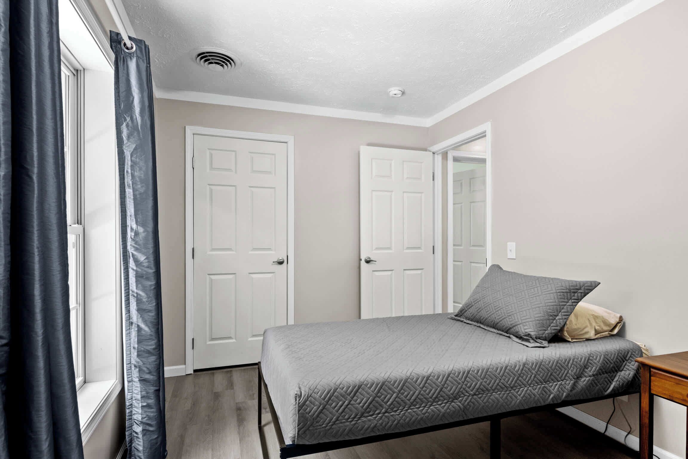 Une chambre à coucher avec un lit, une fenêtre avec des rideaux et deux portes blanches.