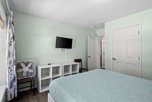 A bedroom with a bed, a TV mounted on the wall, a fan, and a door. - Belle Maison Intermediate Lake Cottage (Bellaire)