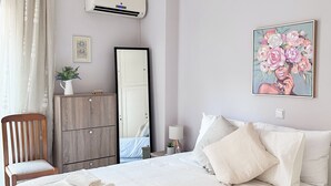A bedroom with a large bed, a wooden chair, a dresser, a mirror, and a painting on the wall.