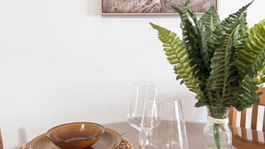 A dining table with a Buddha painting, a woven placemat, a glass vase with a plant, and empty wine glasses.