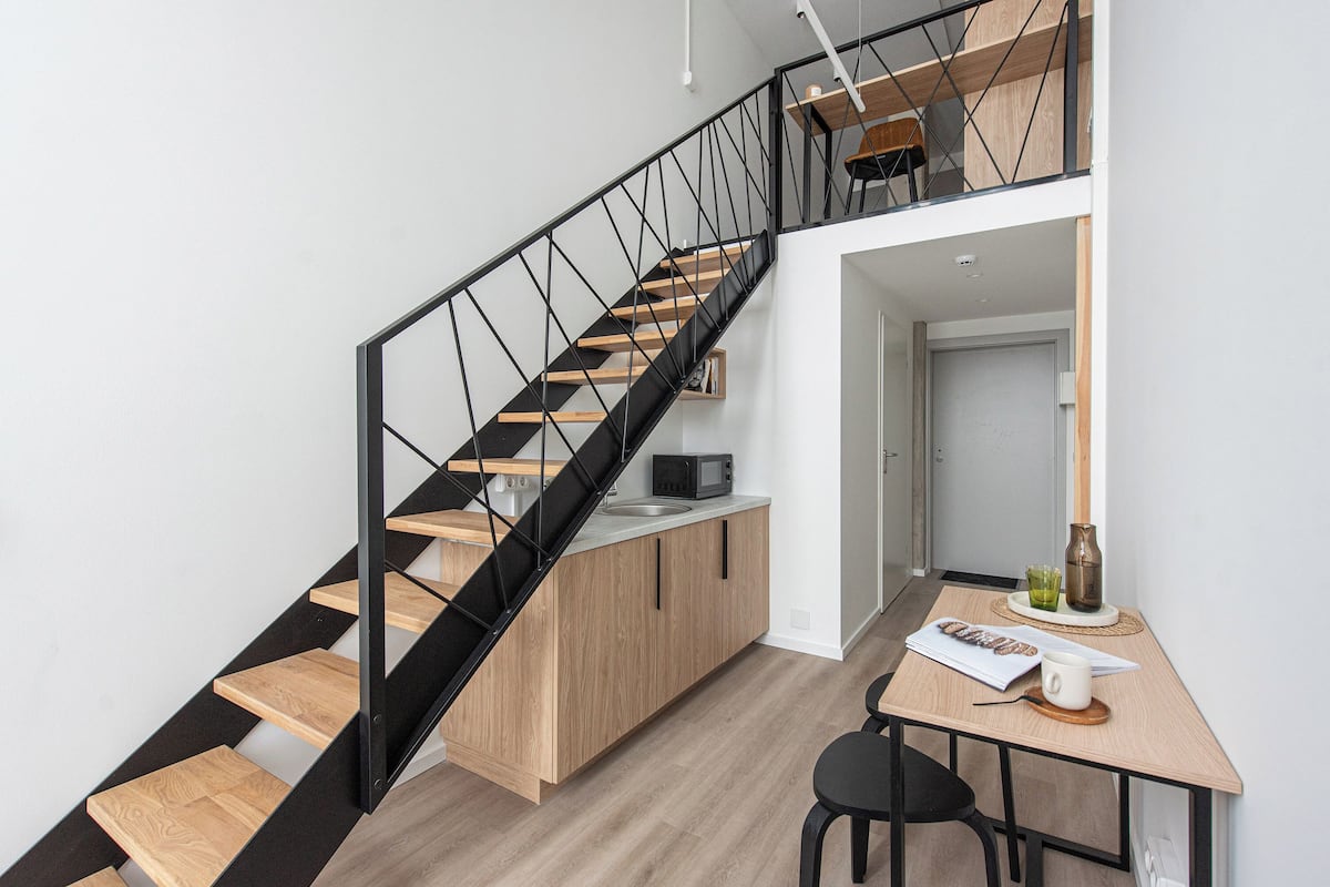 A modern kitchen with a wooden staircase and a dining area.