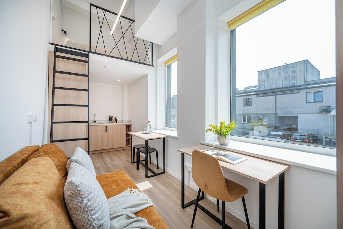 A compact living space with a loft bedroom, a kitchenette, and a desk by a window.