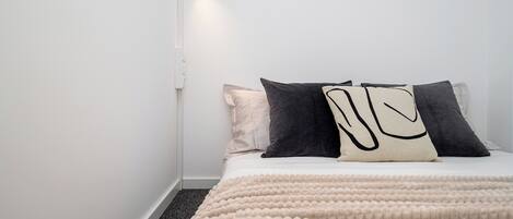 A neatly made bed with a beige blanket and two pillows, one with a black design.