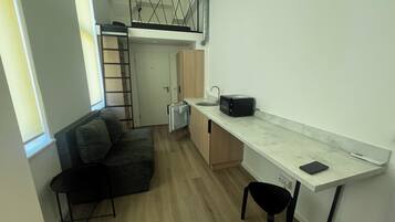 A compact studio apartment with a kitchenette, a loft bed, a sofa, and a dining area.