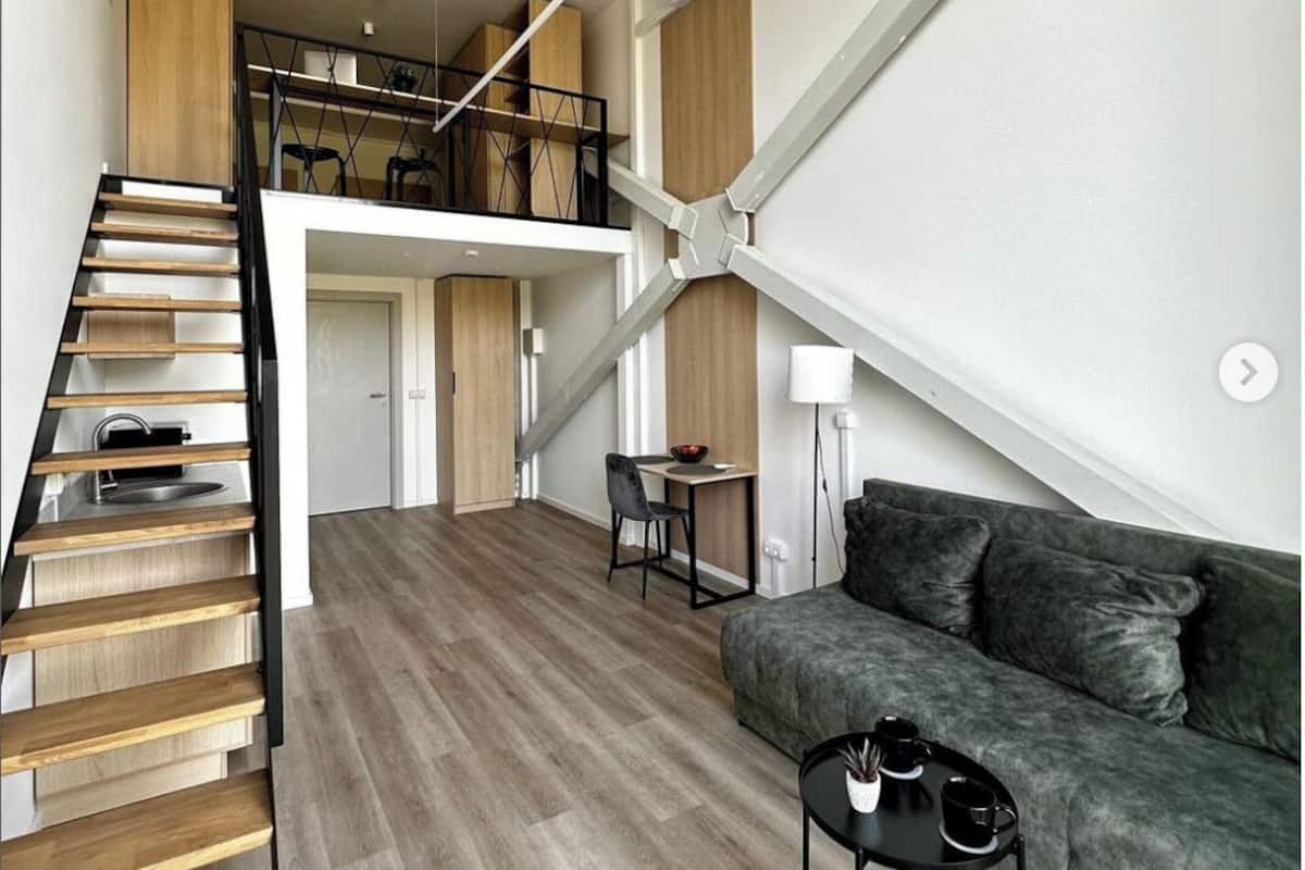 A spacious living area with a staircase leading to an upper level, a grey sofa, and a small table with a lamp.