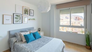 A bedroom with a bed, bedside table, wall art, and a window with a view of buildings. - Apartment Catania in Aguadulce - Almeria. Equipped, elegant, and with sea views (Aguadulce)