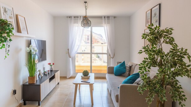 A modern living room with a sofa, a coffee table, a TV, and a large window with curtains. - Apartment Catania in Aguadulce - Almeria. Equipped, elegant, and with sea views (Aguadulce)