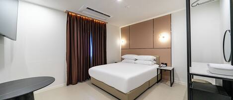 Una habitación de hotel moderna con una cama grande, una mesita de noche, televisor integrado y un baño con espejo y lavabo.