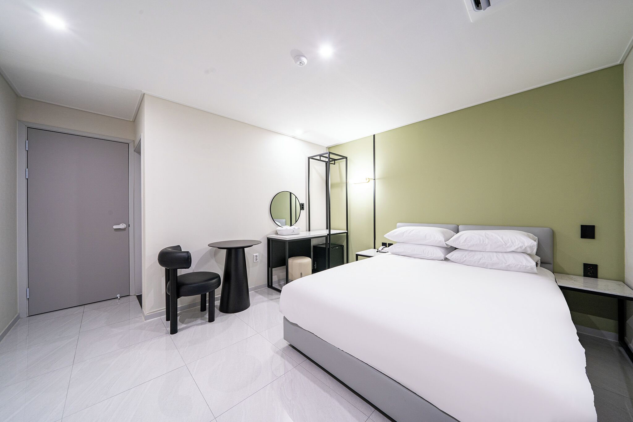 Una habitación de hotel moderna con una cama grande, un escritorio, una silla, un espejo y un armario.