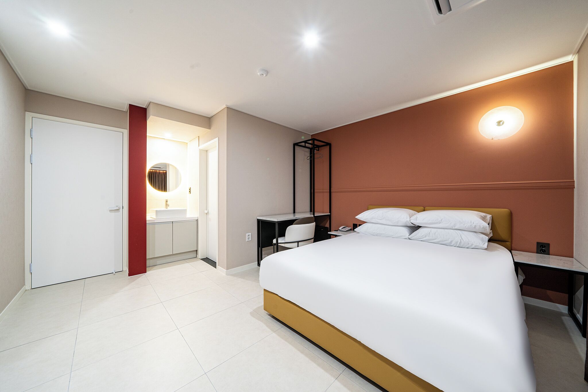 Una habitación de hotel moderna con una cama grande, un escritorio y un baño con espejo y lavamanos.