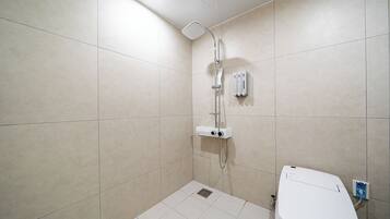 A small, modern bathroom with a shower, toilet, and a control panel on the wall.