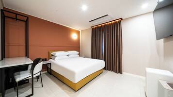 A hotel room with a bed, a desk, a chair, a TV, and an air conditioning unit.