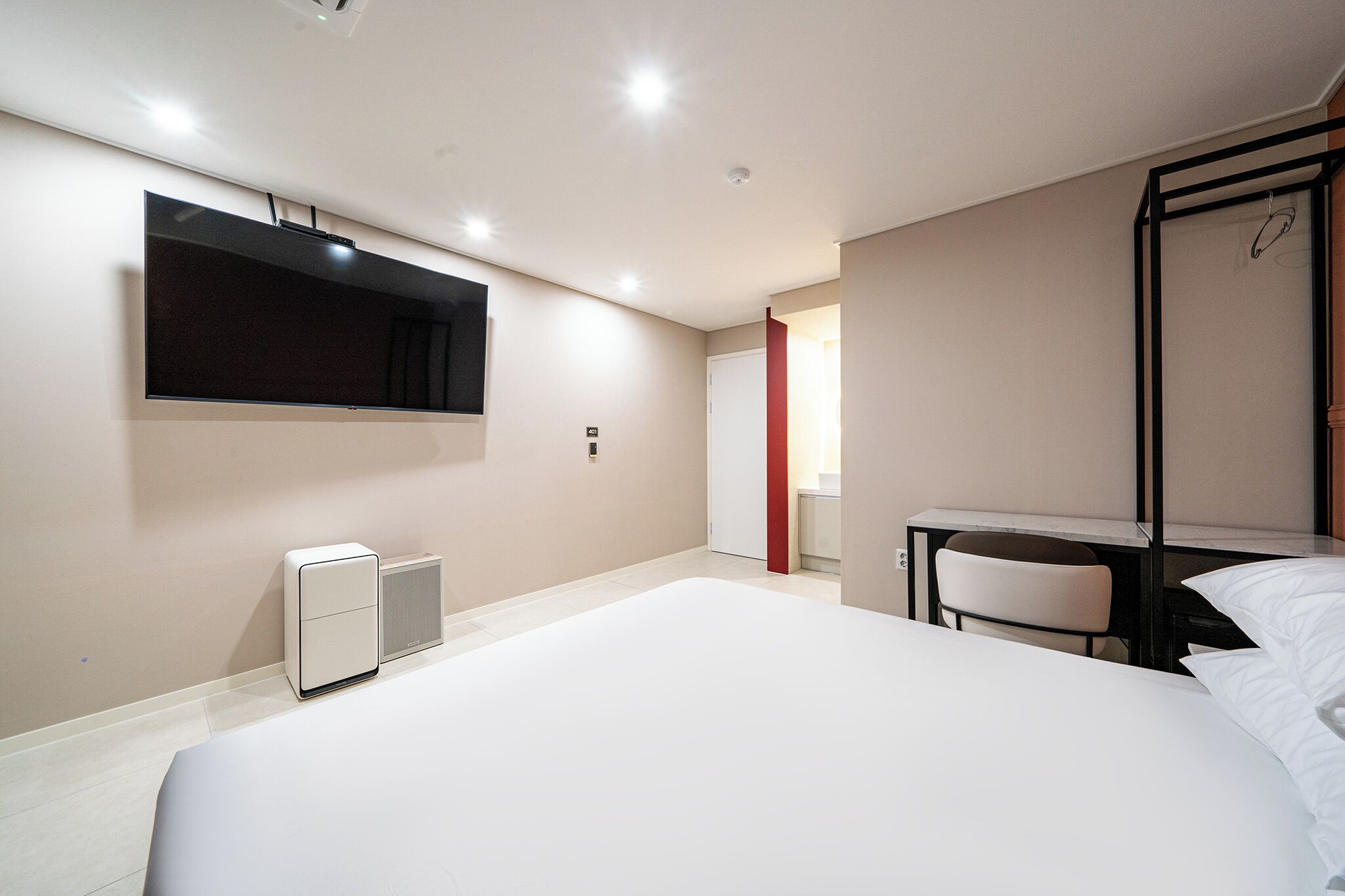 A hotel room with a large bed, a flat-screen TV mounted on the wall, a desk with a chair, and a small heater.