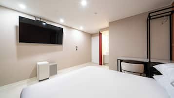 A hotel room with a large bed, a flat-screen TV mounted on the wall, a desk with a chair, and a small heater.