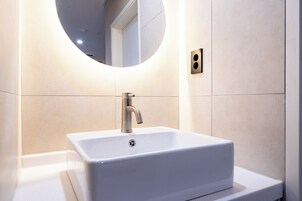 Un baño moderno con un lavamanos rectangular, un espejo redondo y una lámpara empotrada en la pared.