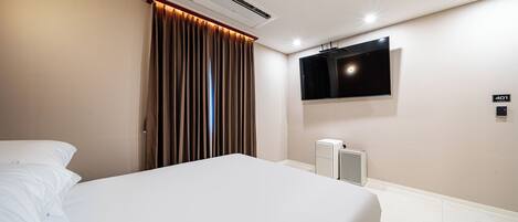 Una habitación de hotel con cama, unidad de aire acondicionado, televisor montado en la pared y panel de control.