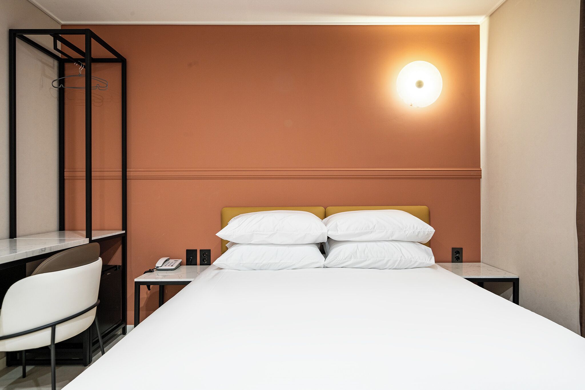 Ein Hotelzimmer mit Bett, Schreibtisch, Stuhl und Nachttisch mit Telefon.