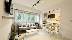 A modern living room with a sofa, dining table, and chairs, a kitchen area with a counter and cabinets, and large windows with curtains. - Spectacular for 2 people in Mar del Plata, steps away from the beach. (Mar del Plata)