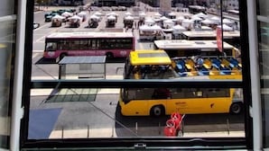Uitzicht vanuit een gebouw op een drukke straat met meerdere bussen en marktkraampjes.