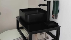 Een badkamer met een zwart wastafel, toilet en spiegel.